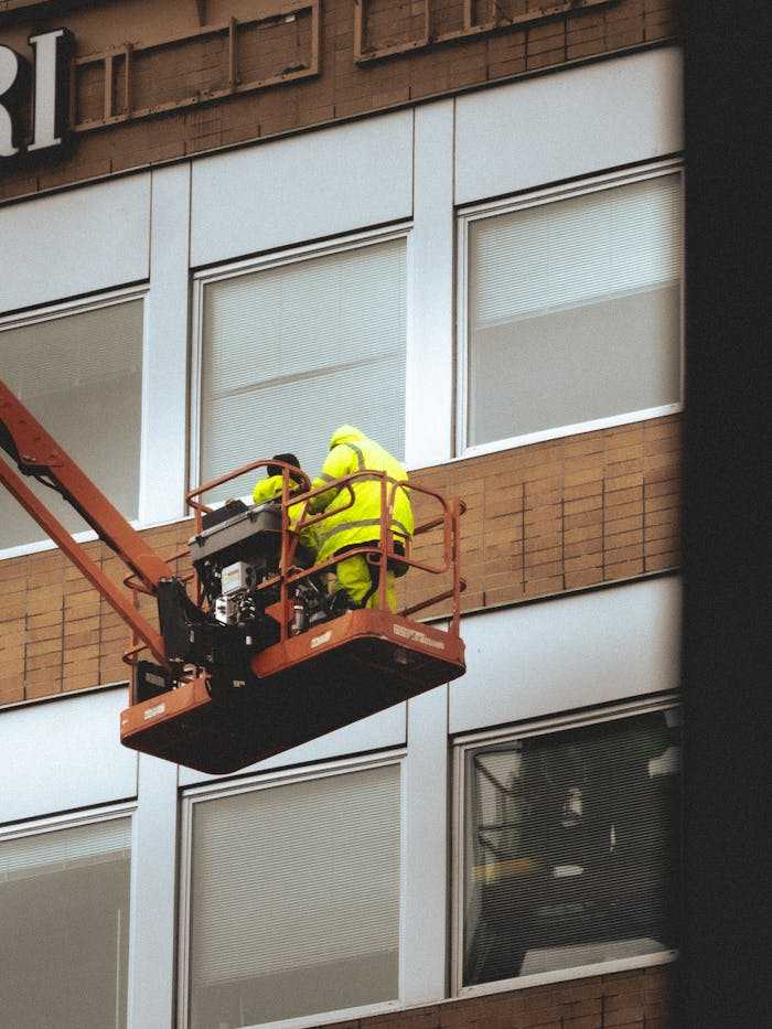 Two workers on a cherry picker doing maintenance on a building façade.